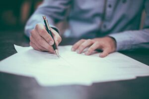 Homme écrivant sur papier, illustrant la rédaction des statuts relatifs au capital social