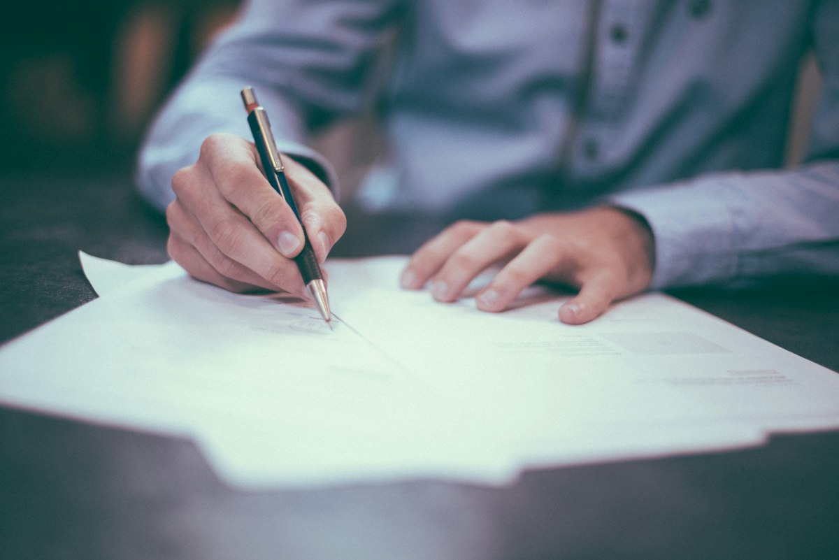 Homme écrivant sur papier, illustrant la rédaction des statuts relatifs au capital social
