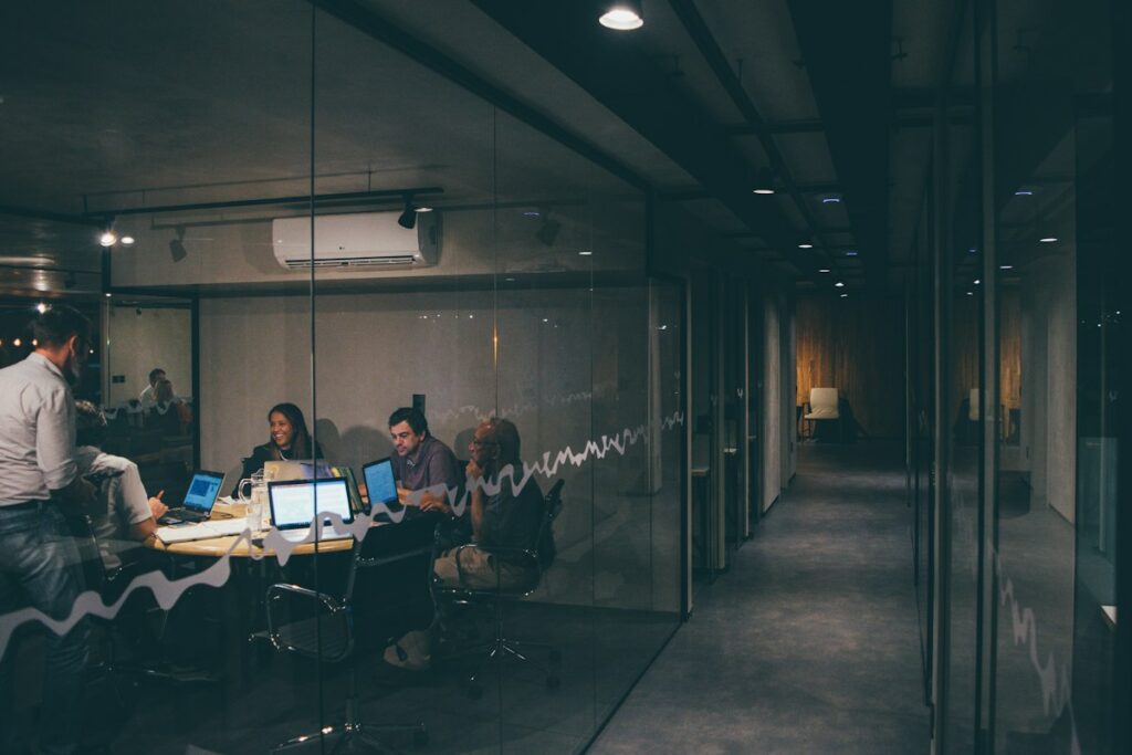 Équipe de fondateurs de startup réunis en salle de réunion vitrée, travaillant sur ordinateurs portables